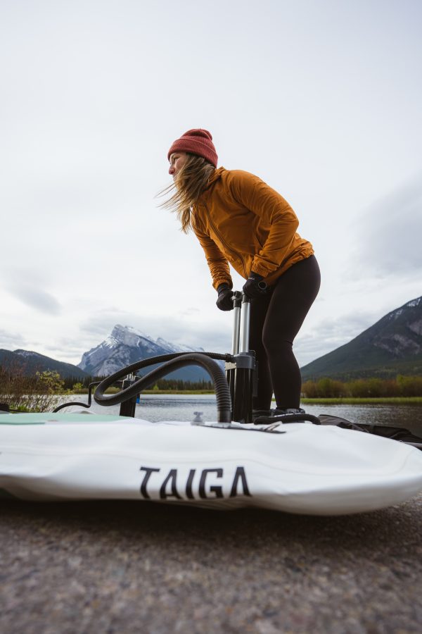 A person paddling on a Taiga Paddle Board in a lake surrounded by mountains and trees