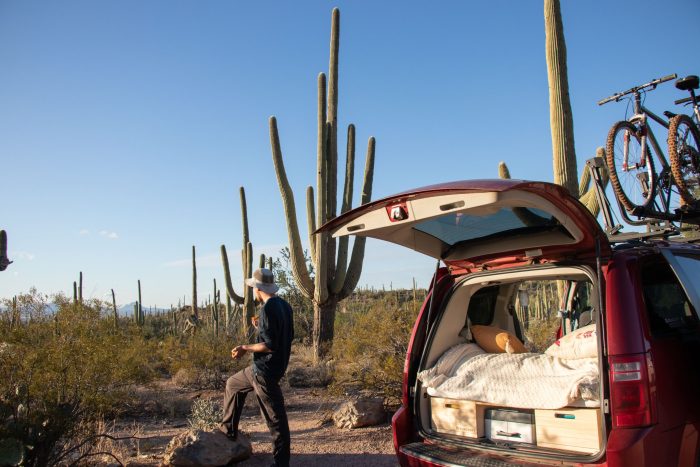 a man standing in the back of a car with a bed in the backRoadloft stealth minivan camper kit, designed for discreet camping and vanlife adventures